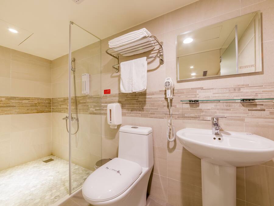 Un bany amb una dutxa de vidre, un vàter, un lavabo i un escurapulides amb tovalloles dobles.