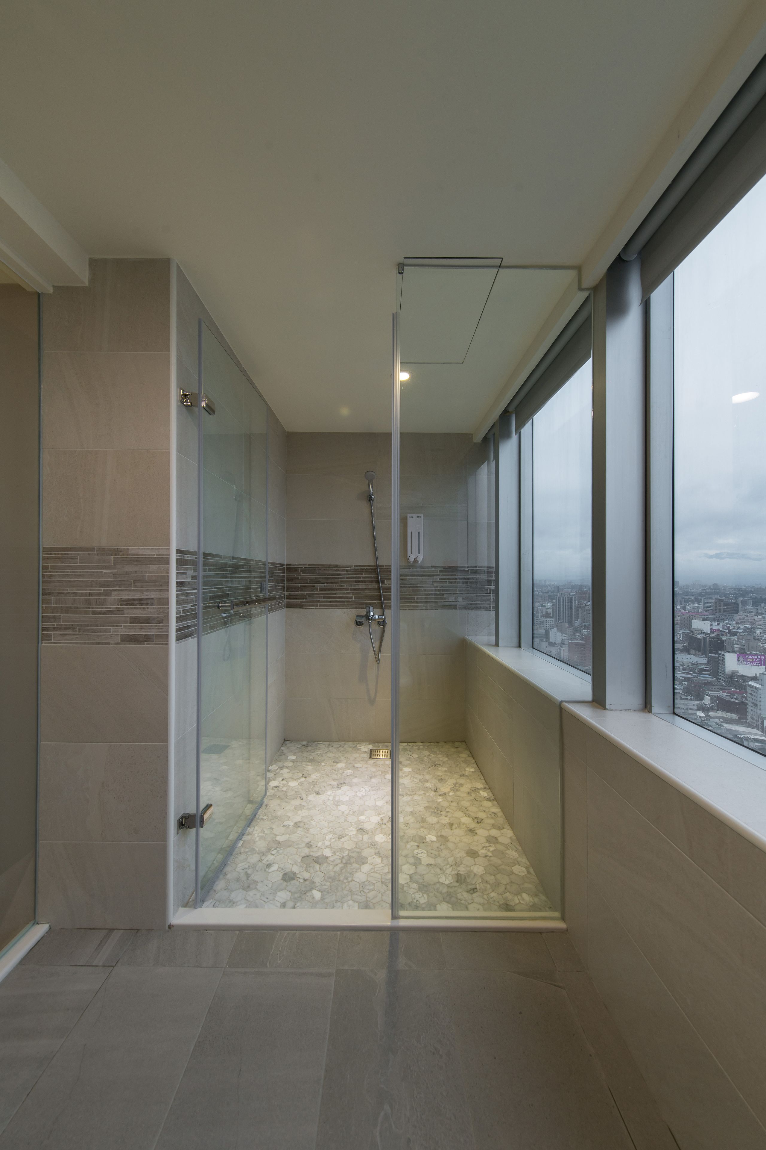 A modern bathroom with a glass-enclosed shower, tiled walls, and a city view through large windows.
