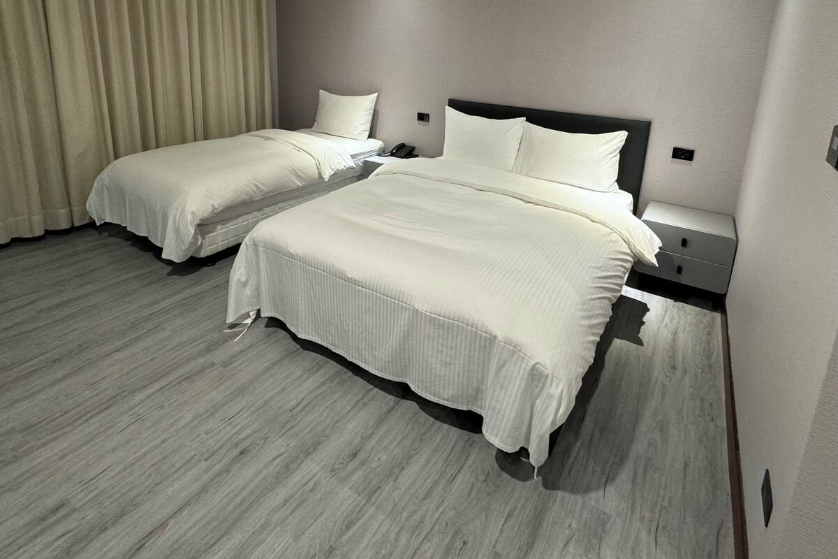 Une chambre d’hôtel avec deux lits, une table de chevet, un téléphone et un interrupteur sur le mur.