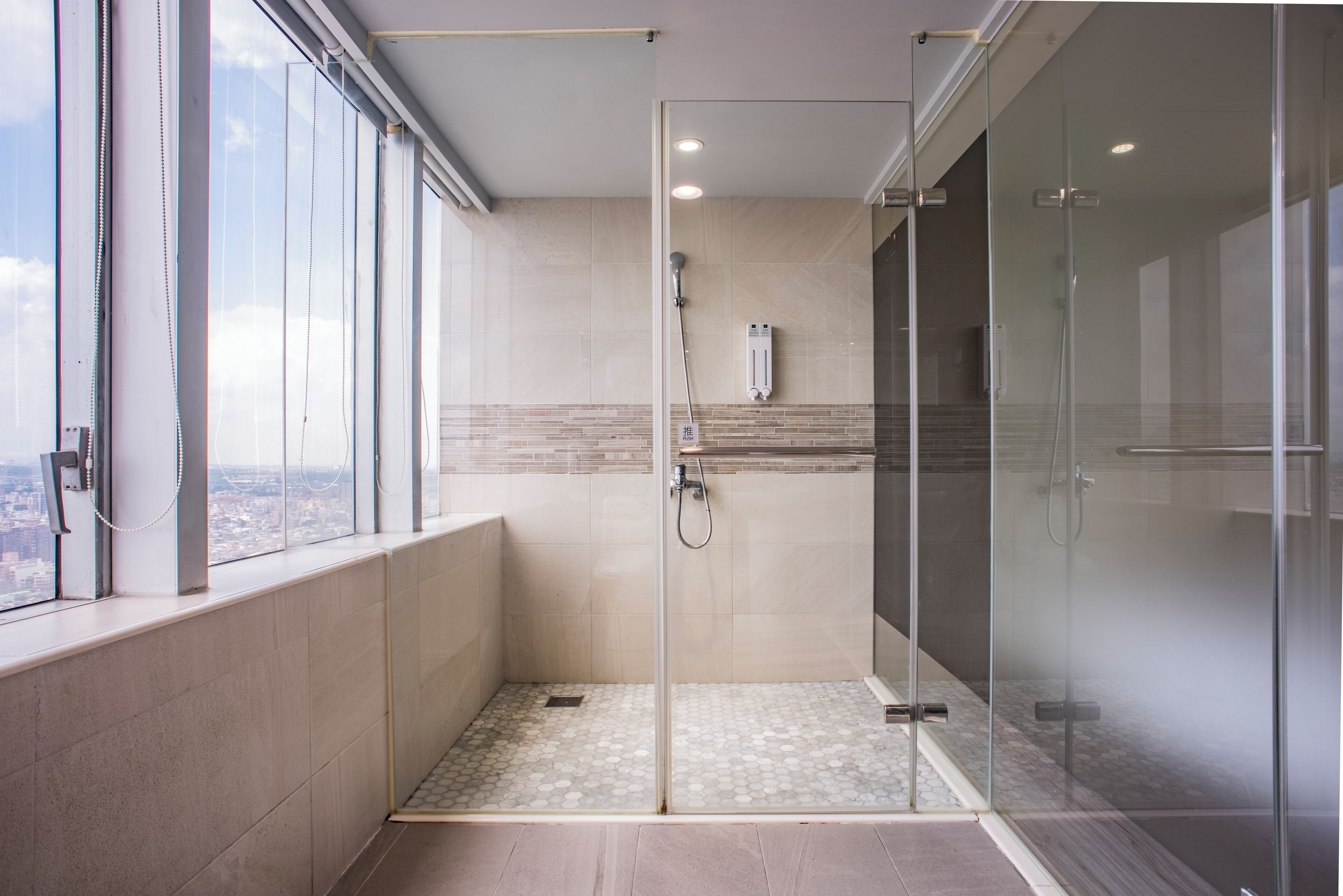 Une salle de bain moderne avec une douche à parois de verre, une vue par la fenêtre et un sol carrelé.
