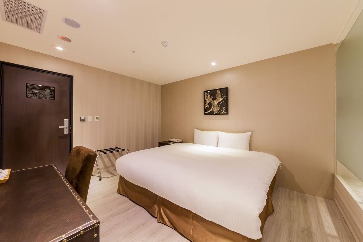Une chambre d’hôtel avec un grand lit, un bureau en bois, une chaise, une table de chevet et une œuvre d’art accrochée au mur.