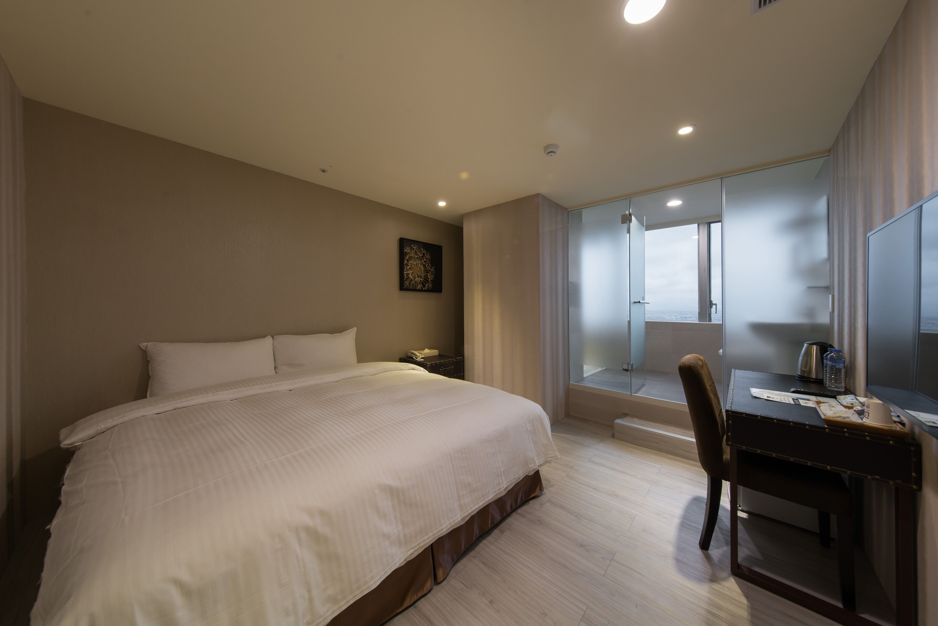 Habitación de hotel con una cama grande, un escritorio con silla, un espejo y una ventana con cortinas.