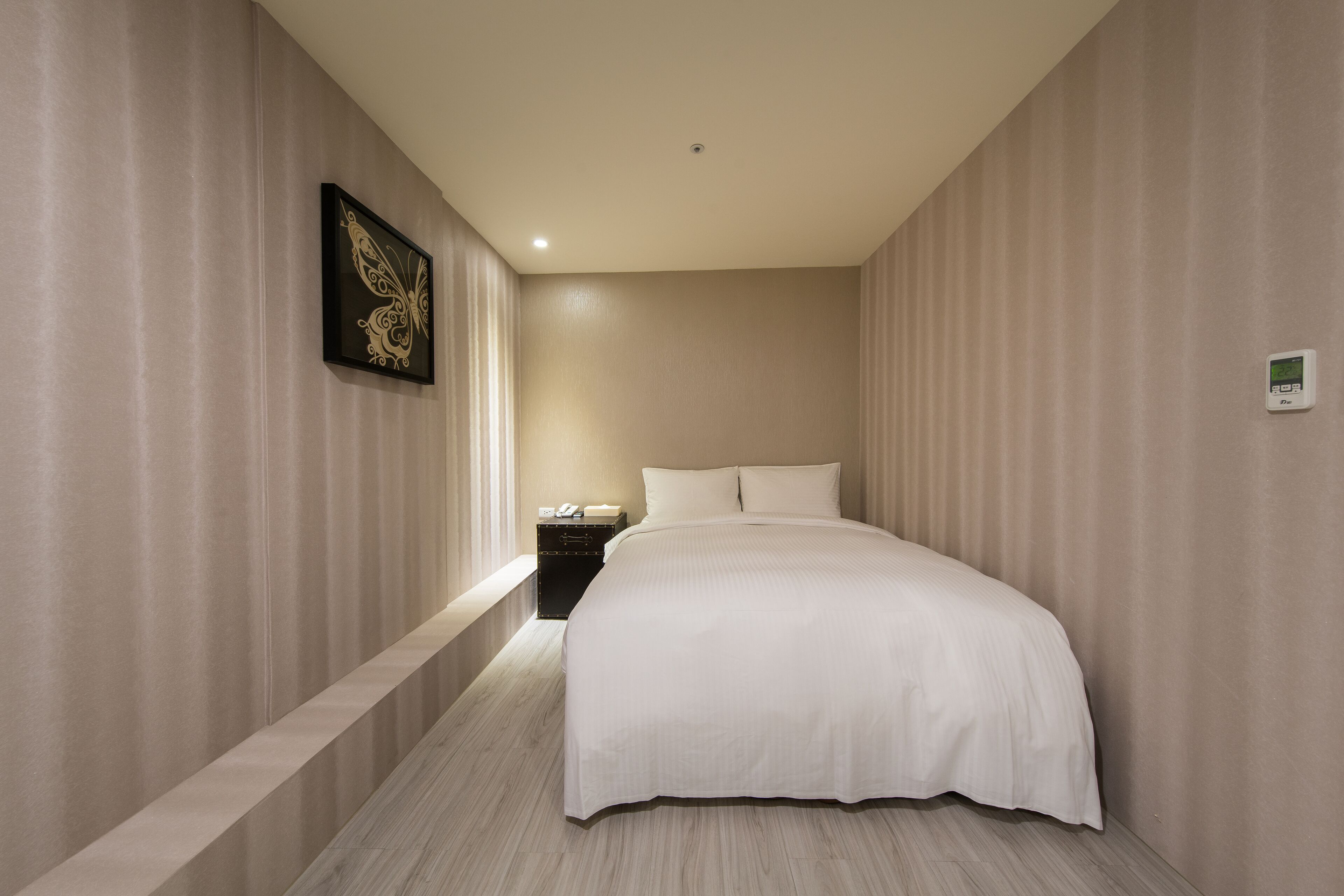 Ein modernes Hotelzimmer mit einem großen Bett, einem Nachttisch und einem an der Wand montierten Thermostat.