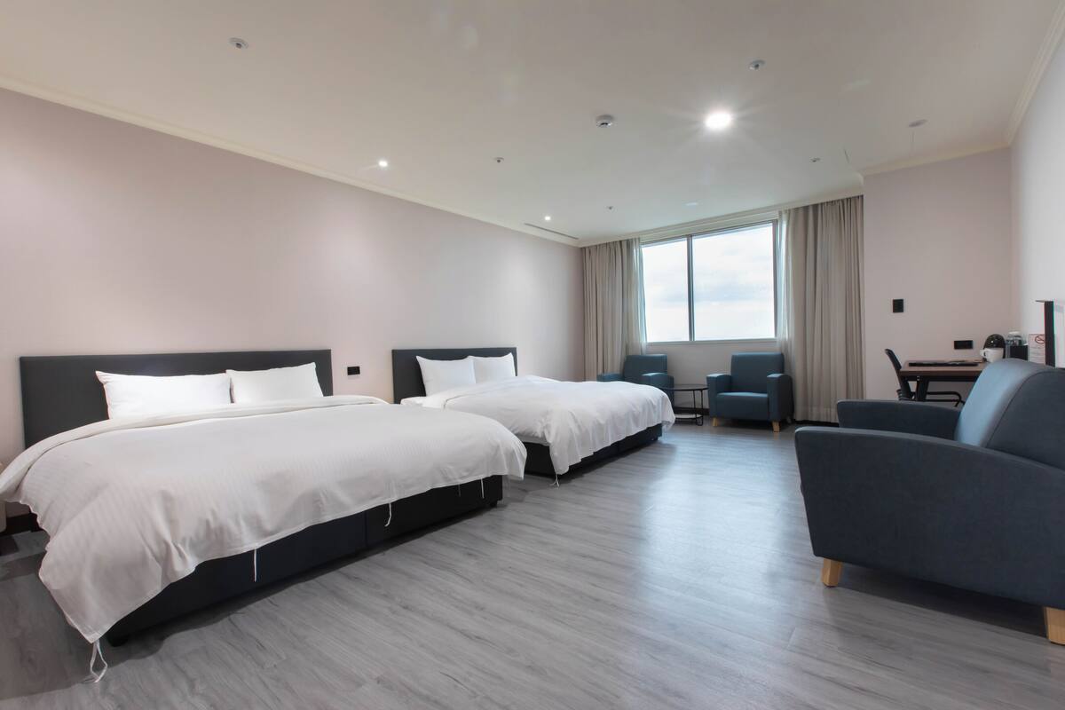 Une chambre d’hôtel avec deux lits, un bureau, une chaise et une grande fenêtre.