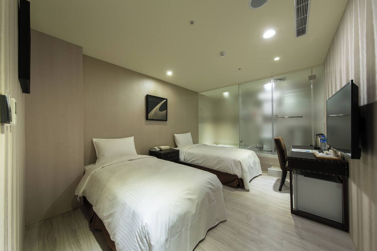 Une chambre d’hôtel avec deux lits, un bureau, une chaise, une télévision et un miroir.