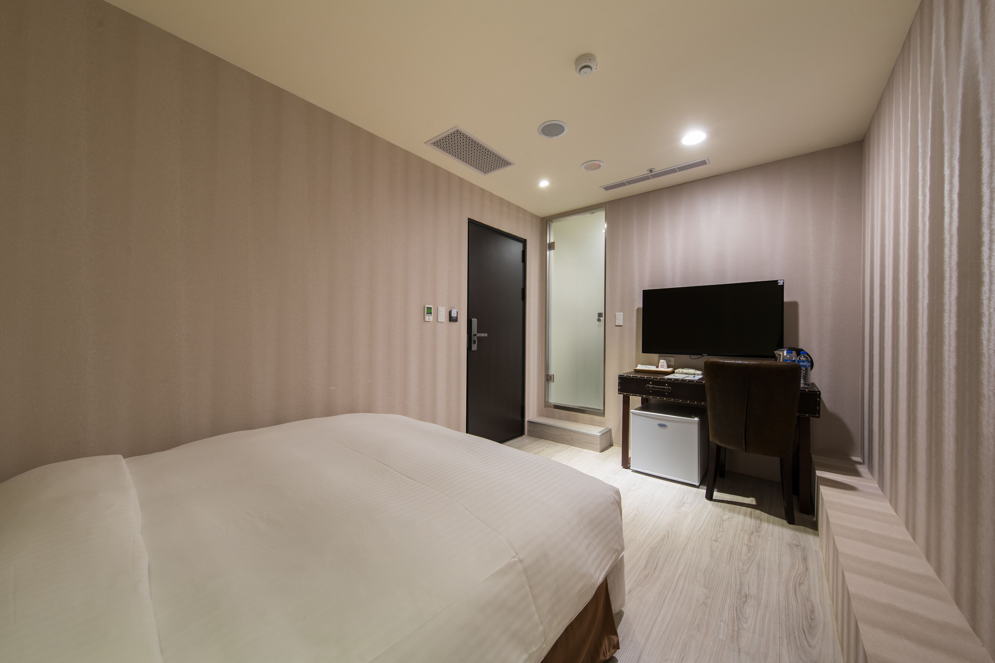 Una habitación de hotel con cama, escritorio, televisor y puerta.