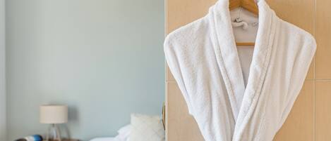 A hotel room with a bed, a bedside table with a lamp, and a robe hanging on a hook.