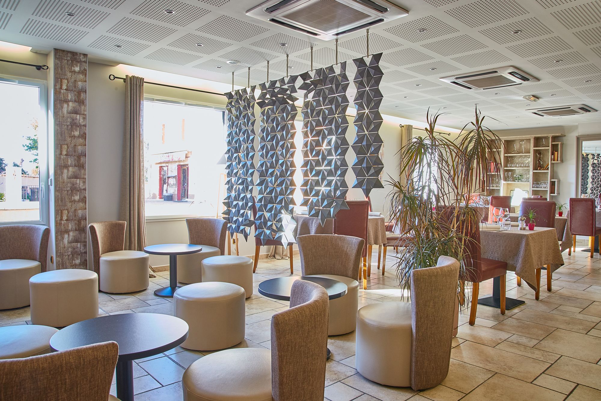 A modern interior with round tables and chairs, a geometric wall feature, and a view of the outside.