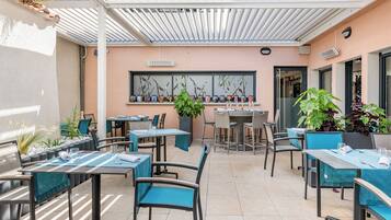 Un patio al aire libre con mesas y sillas, una zona de estar cubierta y una variedad de plantas en macetas.
