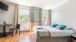 Une chambre d’hôtel moderne dotée d’un grand lit, d’un bureau avec un ordinateur portable, d’une chaise et d’un téléviseur fixé au mur.