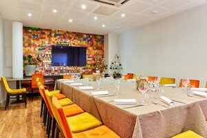 Uma sala de conferências com uma mesa comprida preparada para uma reunião, rodeada por cadeiras laranja.