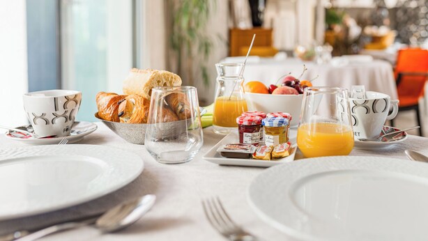 Une table mise pour le petit-déjeuner avec des assiettes, des couverts, du pain, des fruits et du jus.