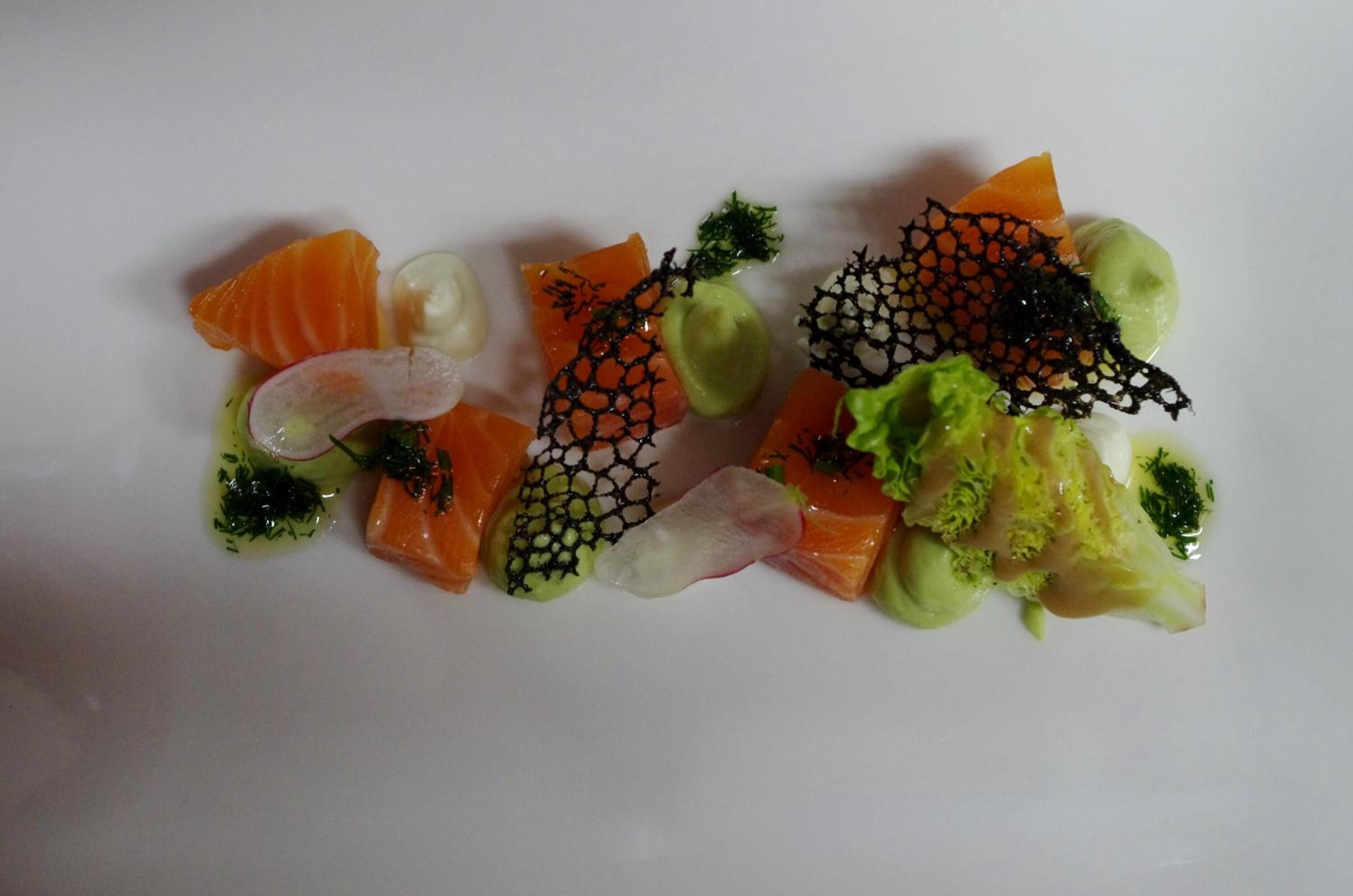 Ein weißer Teller mit verschiedenen Speisen, darunter Lachs, Rettich und Brokkoli.