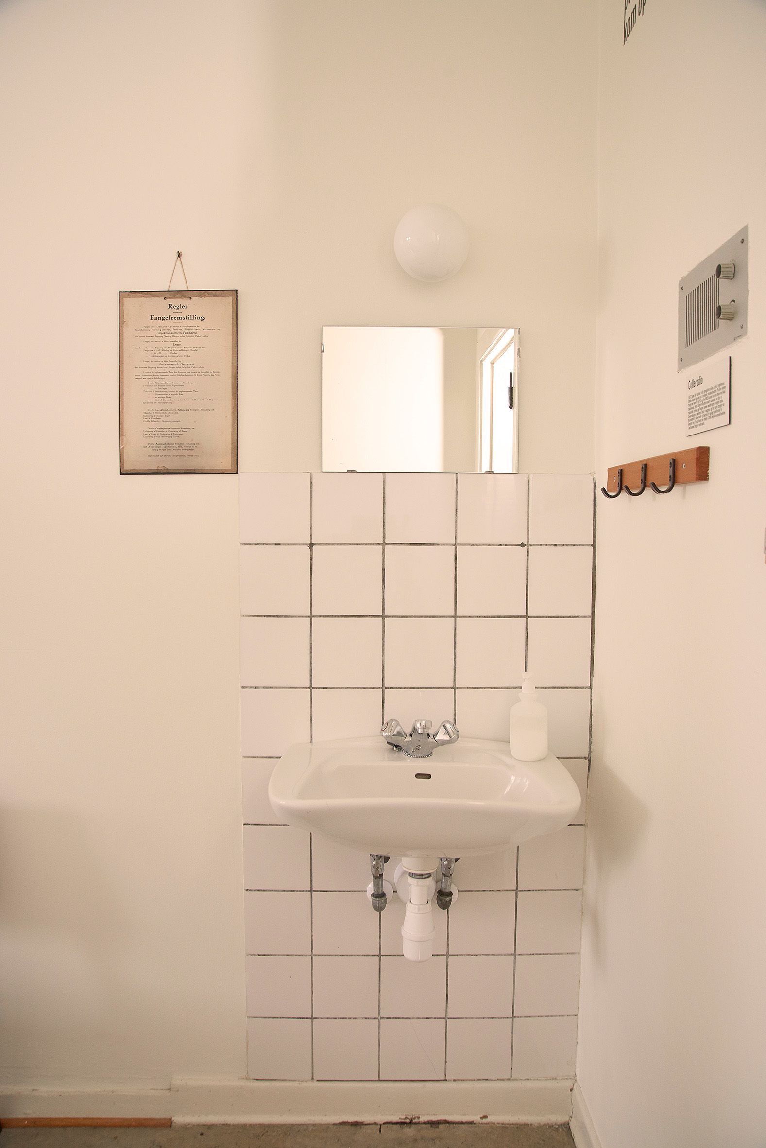 Une salle de bain avec un lavabo blanc, un miroir au-dessus et un mur recouvert de carreaux.