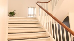 Un escalier avec des rampes blanches et une main courante en bois, menant à l’étage supérieur.