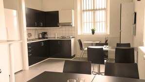 Une cuisine moderne avec des meubles de couleur noire, un coin repas comprenant une table et des chaises, et une fenêtre avec des barreaux.