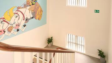 A staircase with a wooden handrail, a mural, and potted plants.