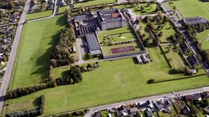 Vue aérienne d’un grand bâtiment institutionnel doté de nombreux terrains de sport, entouré de zones résidentielles.