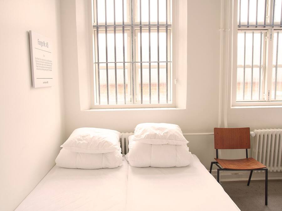 A room with a bed, two white pillows, a wooden chair, and a radiator.