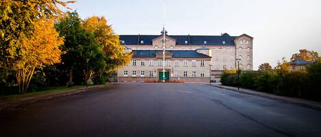 A large, historic building with a symmetrical facade, a central entrance, and a flagpole.