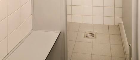 A small, enclosed shower area with white tiled walls and floor, a showerhead, and a handheld shower attachment.
