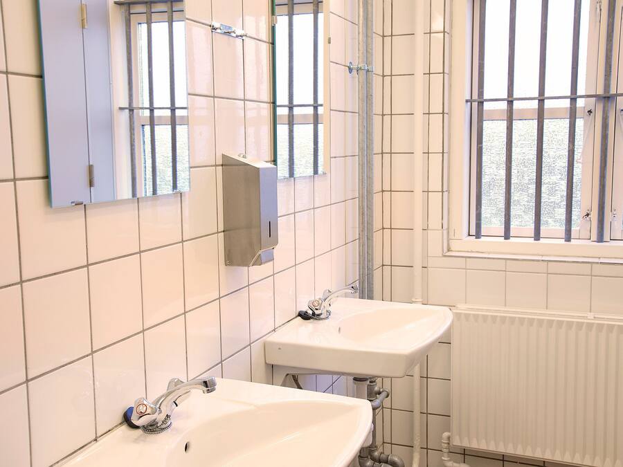 A bathroom with two sinks, a mirror, and a window with bars.