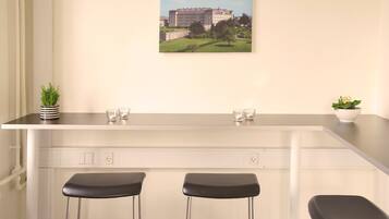 A bar area with a white countertop, two black stools, and a potted plant.