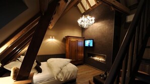 A cozy attic bedroom with a bed, a television, a fireplace, and a chandelier. - B&B De Rentmeesterhoeve (Poperinge)