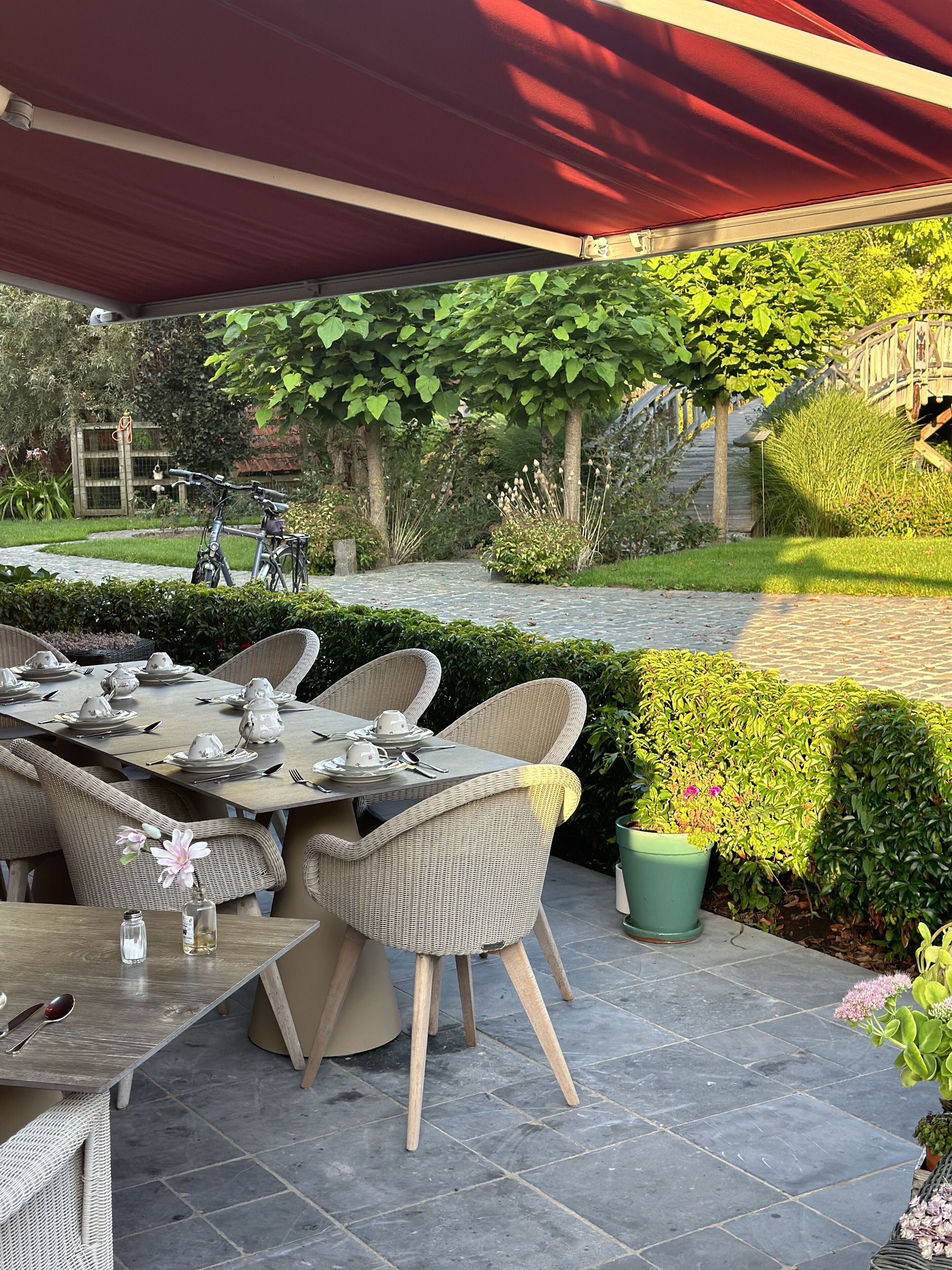 An outdoor patio with a covered dining area, wicker furniture, and a potted plant.