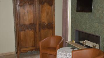 A room with a wooden wardrobe, a leather armchair, a small table with a lace tablecloth, and a flat-screen TV mounted on the wall.