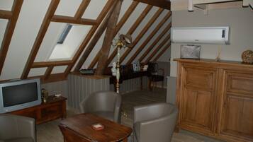 A loft-style room with a sloped ceiling, wooden beams, a television, a small table, two chairs, a cabinet, and a radiator.