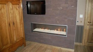 A room with a built-in fireplace, a wooden cabinet, and a television mounted on the wall. - B&B De Rentmeesterhoeve (Poperinge)