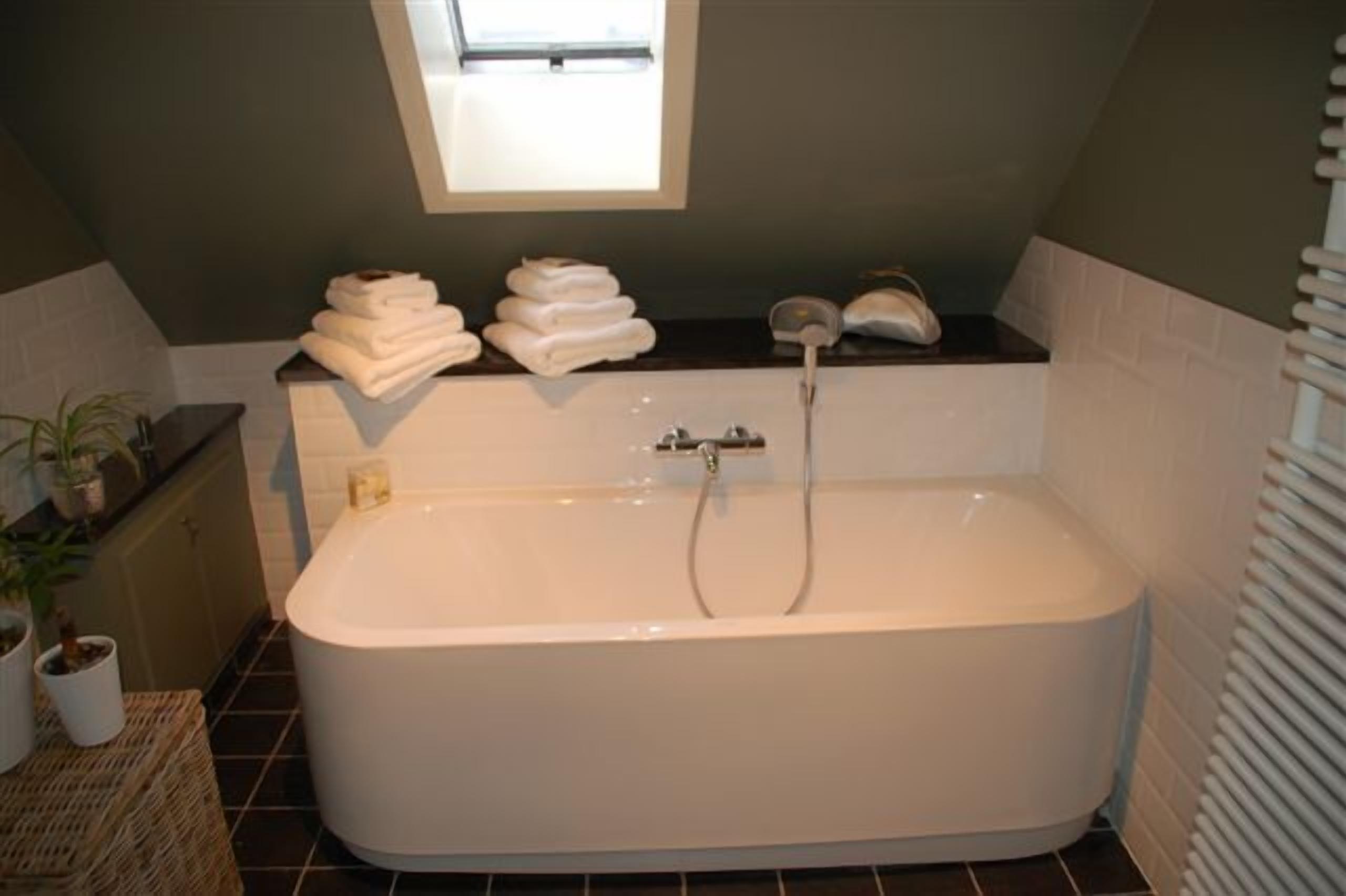 A modern bathroom with a freestanding bathtub, a window above the tub, and a stack of towels on the counter.