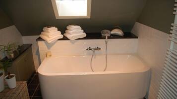 A modern bathroom with a freestanding bathtub, a window above the tub, and a stack of towels on the counter.