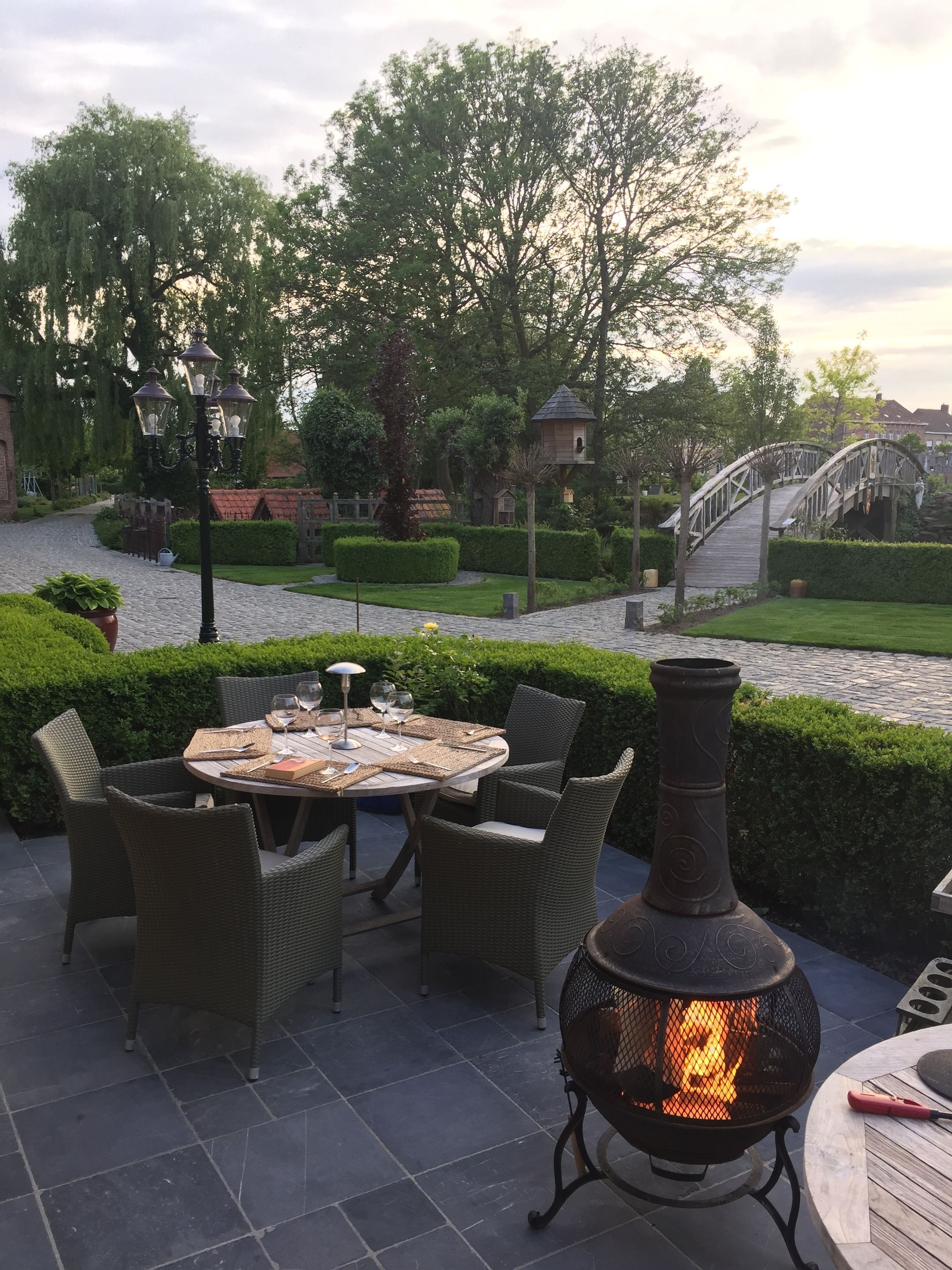 Une terrasse extérieure aménagée avec des meubles en osier, une table dressée pour le repas et un poêle à bois.