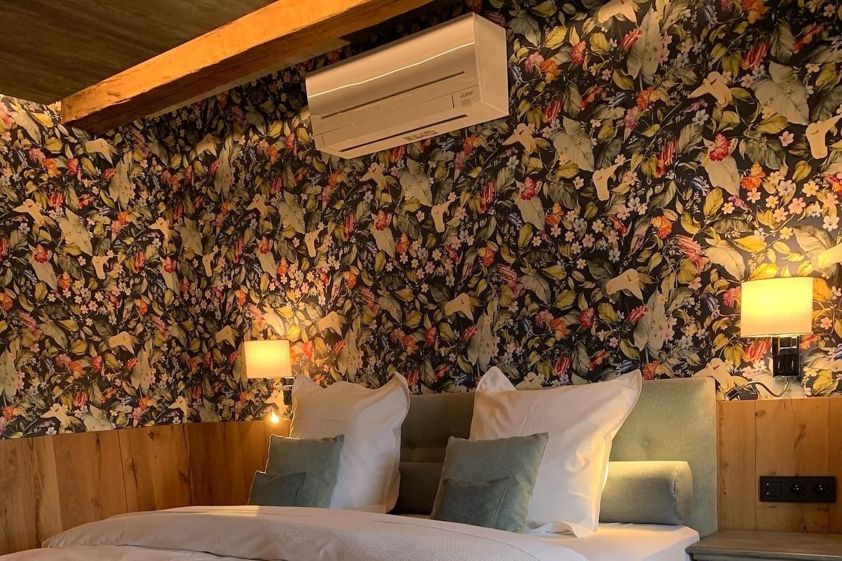 A bedroom with a floral wallpaper, a bed with white bedding, two bedside lamps, and a wooden headboard.