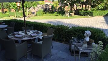 An outdoor patio with round tables and wicker chairs, a statue, and a stone pathway leading to a building.