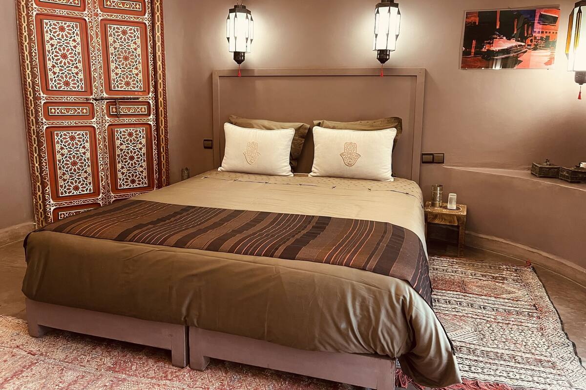 A bedroom with a large bed, two wall-mounted lamps, a decorative door, and a small table with a lamp.
