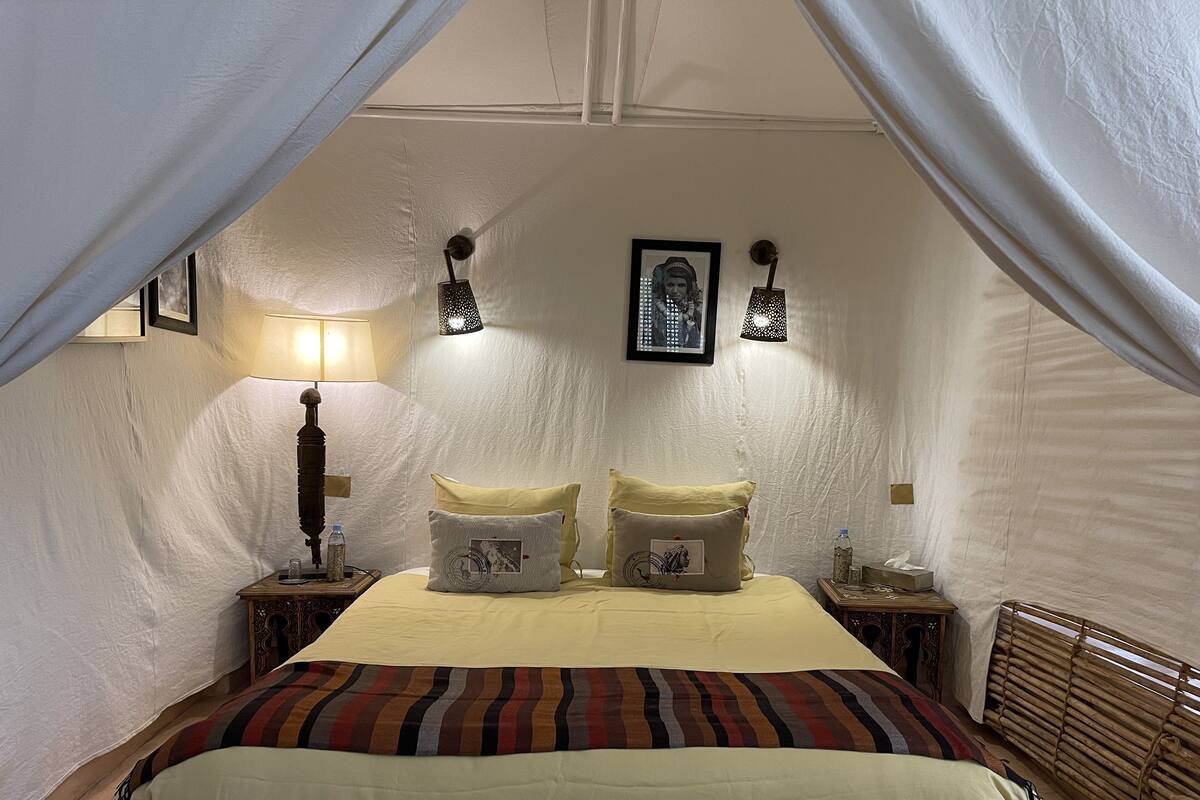 A bedroom with a bed, two bedside tables, a lamp, and a wall-mounted picture frame.
