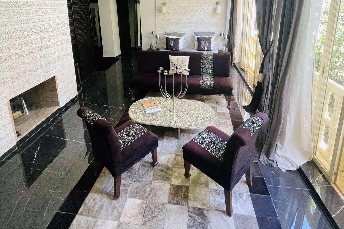 A spacious living area with a high ceiling, a fireplace, a round coffee table, and a sofa with patterned cushions.