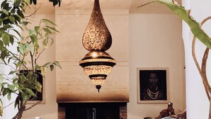A traditional interior with a central fireplace, a hanging ornate chandelier, and two sculptural masks. - Riad 144 (Marrakech)