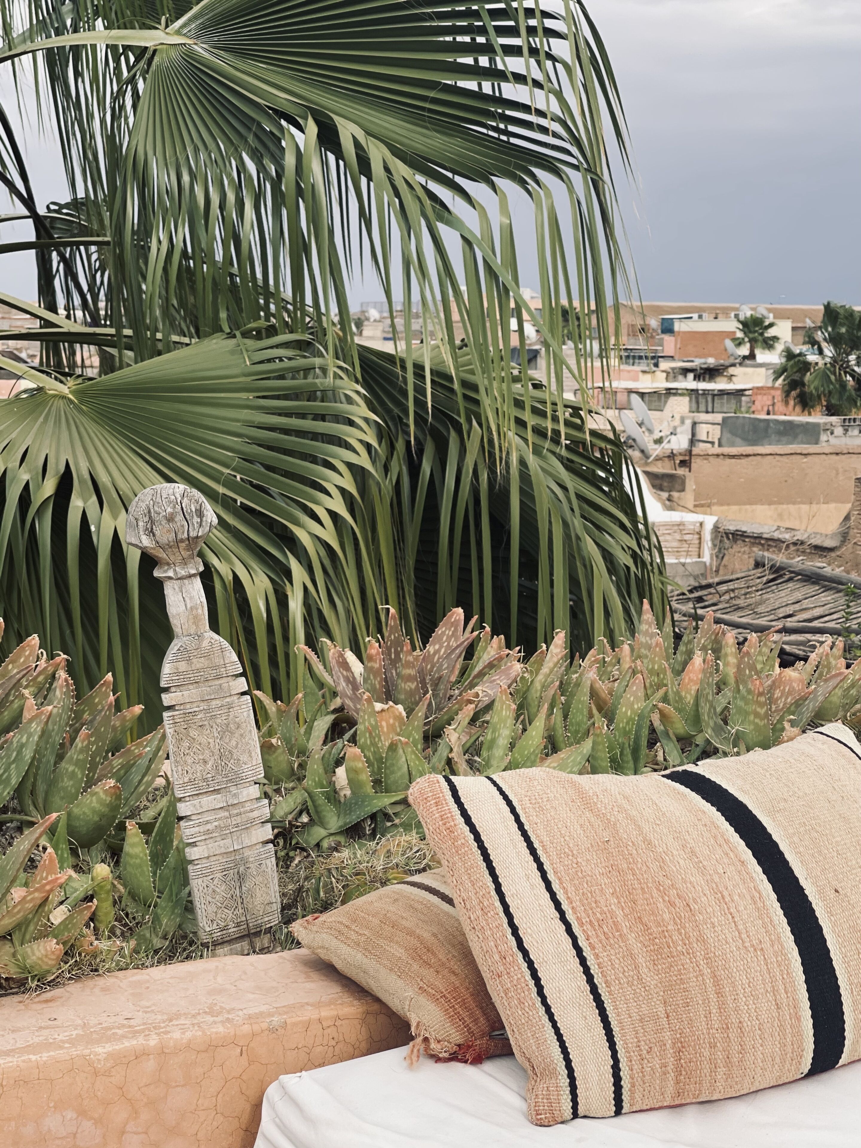 A rooftop garden with a stone sculpture, aloe plants, and a woven cushion.