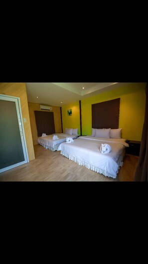 Une chambre d’hôtel avec trois lits, un plancher en bois et des murs jaunes.