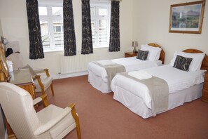 Ett hotellrum med två sängar, ett skrivbord, en stol, en lampa och ett fönster med gardiner.