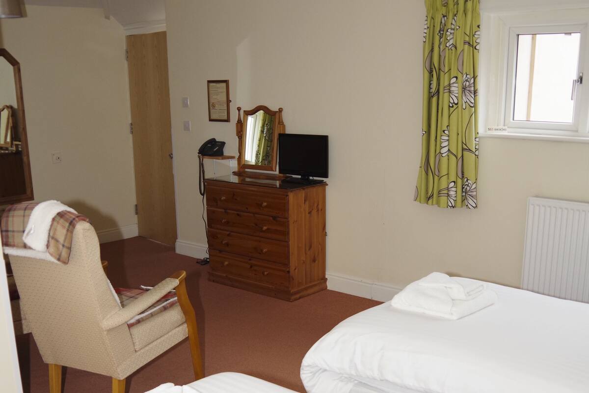 A hotel room with two beds, a chair, a dresser, a television, and a window with curtains.