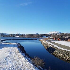 A snow-covered landscape with a calm river, a stone wall, and a few buildings in the background. - Bjugn Hotell (Orland)