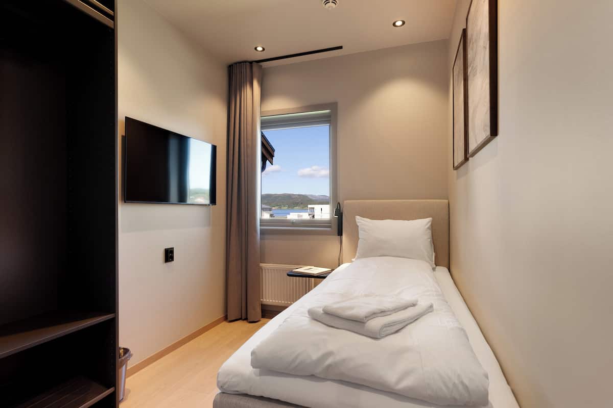 A modern hotel room with a bed, a flat-screen TV, a window with a view, and a radiator.