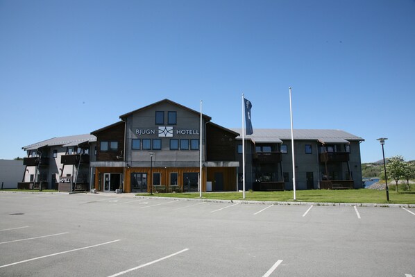 A modern hotel with a prominent sign, a parking lot, and a flagpole. - Bjugn Hotell (Orland)