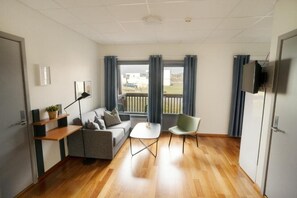 A modern living room with a sofa, a small table, a chair, a TV mounted on the wall, and a window with curtains. - Bjugn Hotell (Orland)