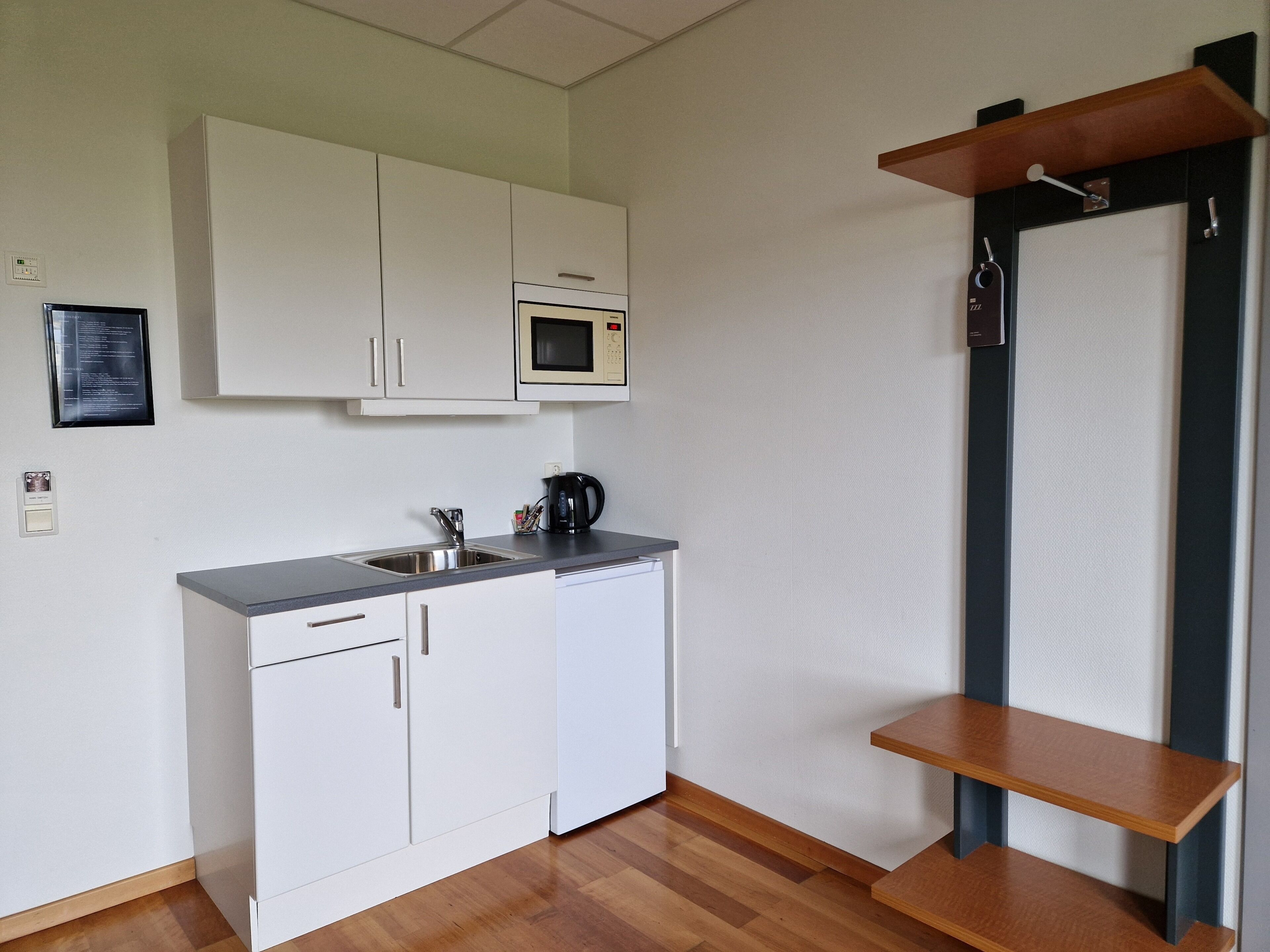 Una cocina compacta con armarios blancos, un microondas, una cafetera y un estante de madera.